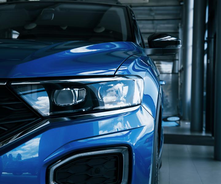 Front part of brand new modern blue car. Parked at showroom. Reflection in the headlights.